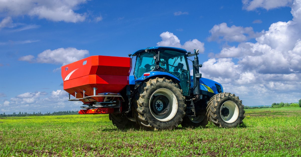  A tracker driving through a field with smaller crops. It has a fertilizer spreader attached to the back end.